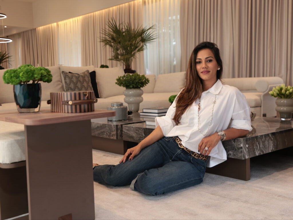 Architect Glaucia Borges sitting on a rug, leaning on a dark marble coffee table. In the background is a cream-colored sofa. architetti interior design